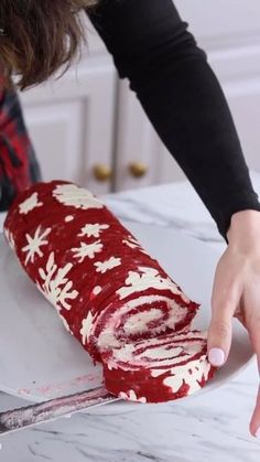 a woman is decorating a roll with red and white frosting on the counter