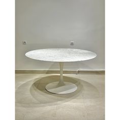 a white table with a circular base in the middle on a tiled floor next to a wall