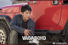 a young man sitting on the ground next to a red truck and looking at something