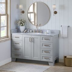 a white bathroom with two sinks and a round mirror on the wall next to a window