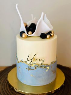 a white and blue cake with gold decorations on it's top, sitting on a wooden table