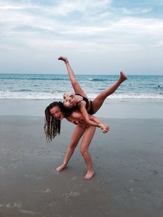 two girls are playing on the beach with their arms in the air and one girl is upside down