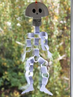 a paper skeleton hanging from a window with trees in the backround behind it