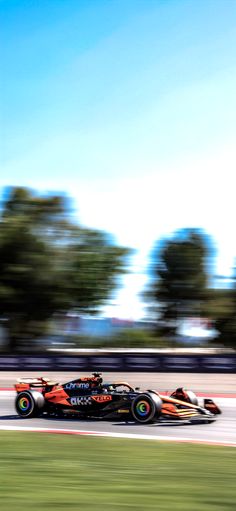 a red and black race car driving on a track with trees in the back ground