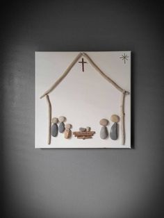 a cross and some rocks in front of a wall hanging on a gray wall with a white frame