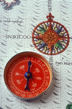 a red compass sitting on top of a map next to a blue and white clock