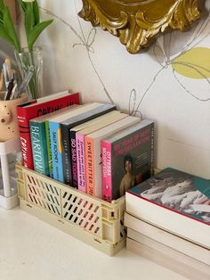 some books are sitting on a shelf next to a vase with flowers and a mirror