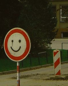 a red and white sign with a smiley face on it in front of some trees