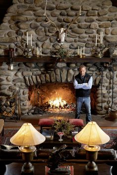 a man standing in front of a fire place with candles on the mantle and deer heads above it