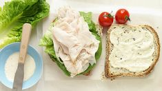 a sandwich with lettuce, tomato and mayonnaise next to a bowl of dressing