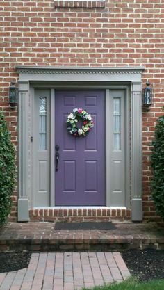 a purple front door with a wreath on it and brick walkway leading up to it