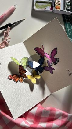 a card with butterflies on it next to some crayons and pens, scissors