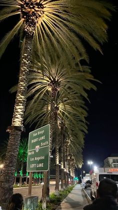 palm trees line the street at night in front of a white van and people walking down the sidewalk