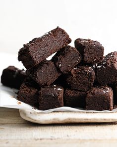 a pile of brownies sitting on top of a white plate next to a wooden table