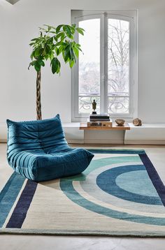 a living room with a blue chair and a potted plant on the floor in front of a window