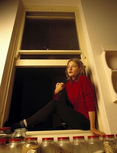 a woman sitting on the window sill in front of some jars and spices,