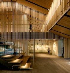 a person walking down the stairs in a building with wooden walls and ceiling lights on either side