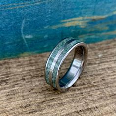 a wedding ring with green and silver inlays sitting on a piece of wood