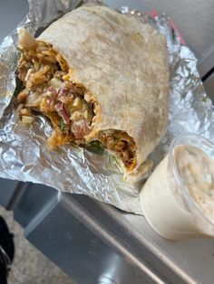 a burrito sitting on top of aluminum foil next to a container of mayonnaise