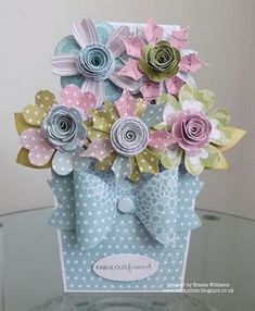 a card with paper flowers in a blue gift bag on a glass table, ready to be used as an ornament