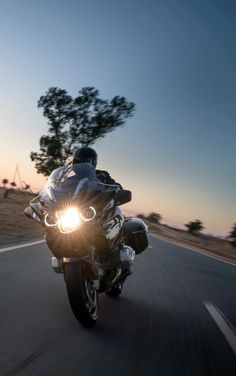 a person riding on the back of a motorcycle down a curvy road at sunset