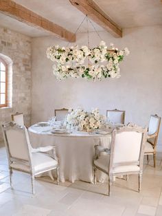 a dining room table with white chairs and flowers hanging from the ceiling