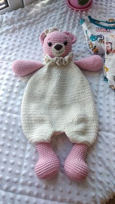 a crocheted teddy bear laying on top of a bed next to a pillow