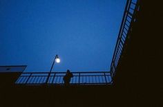 a person standing on a balcony with a street light in the background at night time