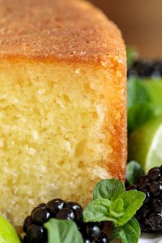 a piece of cake sitting on top of a white plate next to blackberries and limes