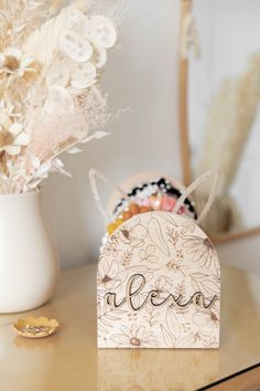 a wooden sign sitting on top of a table next to a vase filled with flowers