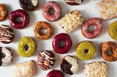 many different types of donuts on a white surface with sprinkles and frosting