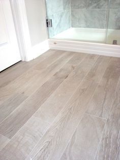 an empty bathroom with wood flooring and glass shower stall in the backround