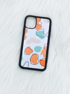 an iphone case sitting on top of a white fur covered surface with orange, blue and green shapes