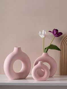 two pink vases sitting on top of a white shelf next to a purple flower