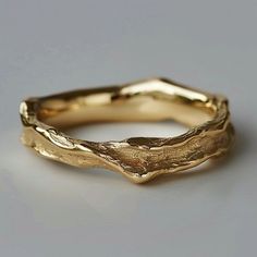 a gold wedding band that has been carved into the shape of a tree branch, on a gray surface