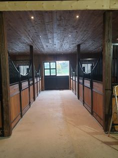 the inside of a horse barn with wooden stalls and doors leading to an open door