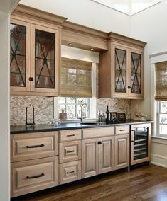 a kitchen with wooden cabinets and black counter tops in front of a window that has roman shades on the windowsills