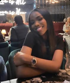 a woman sitting at a table with her arms crossed in front of the camera and smiling