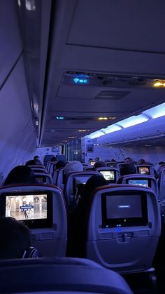 the inside of an airplane with many seats and televisions on each side of the aisle