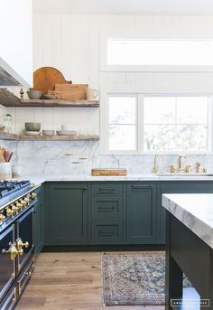 a kitchen with green cabinets and marble counter tops, an island in front of the stove