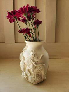 a white vase filled with red flowers on top of a table