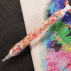 a cross stitch pattern with a colorful toothbrush on it's side next to a needlepoint pen