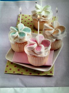 three cupcakes on a plate with candles in the shape of hearts and flowers