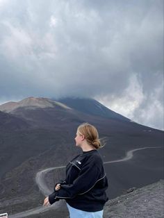 a woman standing on top of a mountain looking up at the clouds in the sky