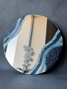 a round mirror with blue and white designs on the front, against a gray wall