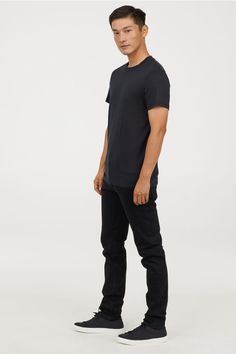 a man standing in front of a white background wearing black pants and a black t - shirt