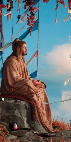 a man with long hair sitting on top of a rock