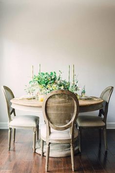 a dining room table with chairs and flowers on the centerpiece, in front of a white wall