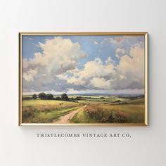 a painting hanging on the wall above a dirt road in front of a cloudy sky