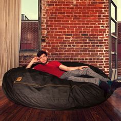 a man laying on top of a bean bag chair in front of a brick wall